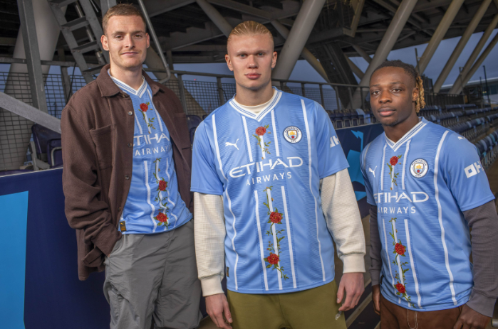 Man City stars Sergio Gómez, Erling Haaland and Jérémy Doku model the limited edition “The Roses and the Bees” jerseys, which feature hand-painted elements by artist Christian Jeffery. Source: Manchester City